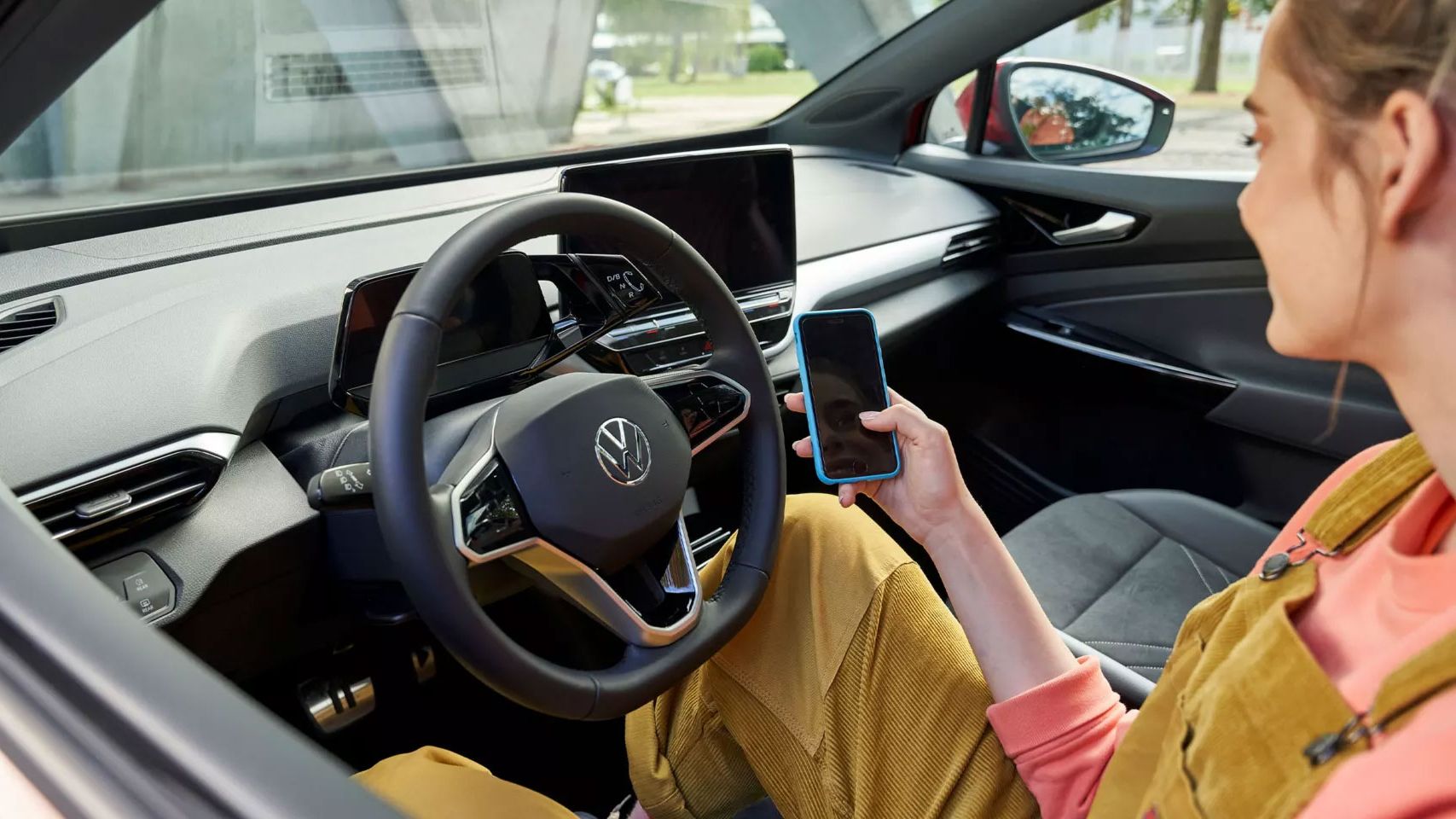 Blick in das Cockpit eines VW ID., eine Frau sitzt darin und blickt auf ihr Smartphone